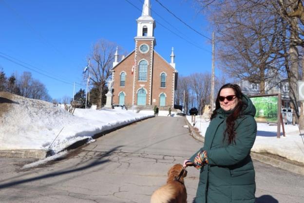 A man smiles standing in front of a church. She is holding the leash attached to her dog. 