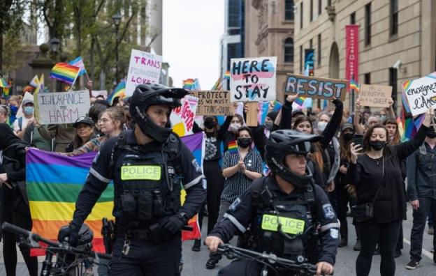 A group of people holding signs are shown in behind police officers.