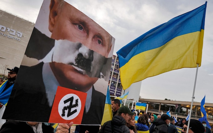 A demo<em></em>nstrator holds up a sign depicting the superimposed face of Russian president Vladimir Putin atop the signature toothbrush moustache of Nazi Germany's leader Adolf Hitler during a protest against Russia's invasion of Ukraine