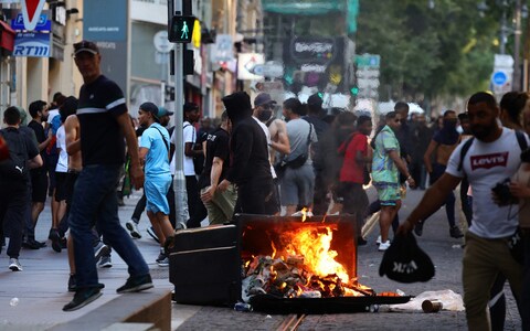 People walk past a burning trash bin after a clash between protesters and police in Marseille on July 1