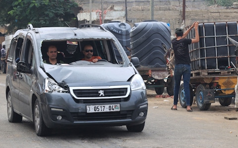 Palestinian men drive past people waiting to collect water using horse- and donkey-drawn carts in Rafah in the southern Gaza Strip