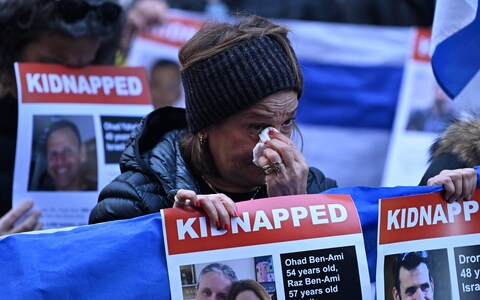 People hold up Israeli flags and posters of the missing as they gather outside the Qatari Embassy