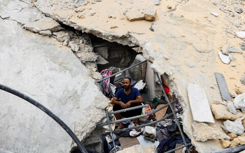 A Palestinian man sits amidst the rubble at the site of Israeli strikes on houses