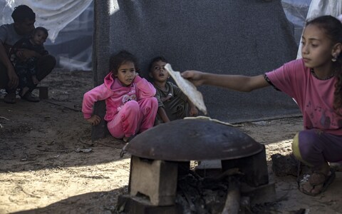 Palestinians wait as bread is being prepared after a rainy night inside a tent complex at a camp 