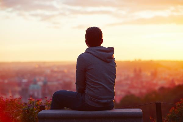 A young man in a hoodie looks out o<em></em>nto the sunrise