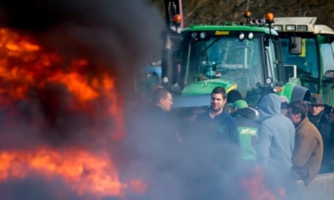 Flames are seen in the foreground as farmers with tractors block a highway