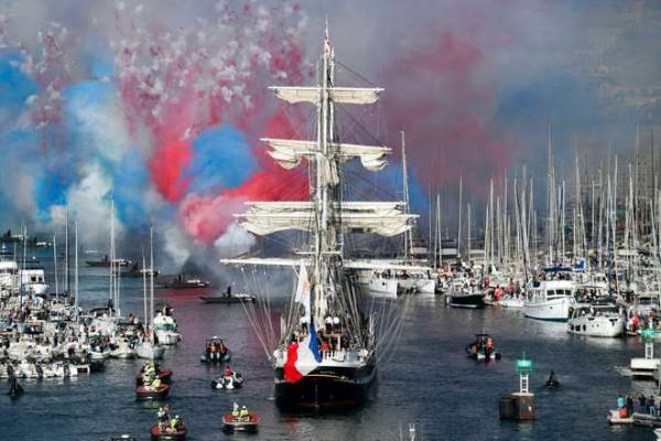 French 19th-century three-masted barque Belem (C) arrives at the Vieux-Port (Old Port) as red white and blue fireworks are fired, during the Olympic Flame arrival ceremony, as part of its journey ahead of the Paris 2024 Olympic and Paralympic Games, in Marseille, southeastern France, on May 8, 2024. The transfer of the flame o<em></em>nshore from a 19th-century tall ship will mark the start of a 12,000-kilometre (7,500-mile) torch relay across mainland France and the country's far-flung overseas territories. (Photo by Sylvain THOMAS / AFP) (Photo by SYLVAIN THOMAS/AFP via Getty Images)