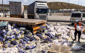 A worker clears spilled goods from damaged trailer trucks that were carrying humanitarian aid on the Israeli side of the Tarqumiyah crossing with the West Bank, on Monday