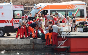 Emergency services carry a body bag after a sailboat sank in the early hours of Monday, off the coast of Porticello, near the Sicilian city of Palermo, Italy