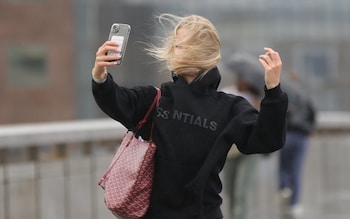 A woman struggles with her hair as she attempts to take a selfie during windy weather in Central London