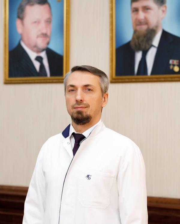 Elkhan Suleymanov, a doctor and former deputy prime minister of Chechnya, stands in front of two portraits, one of warlord Ramzan Kadyrov