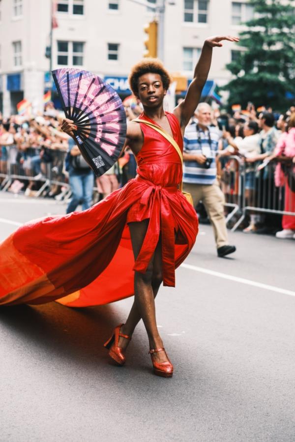 A parade goer wears a red dress as he marches down the parade rout.