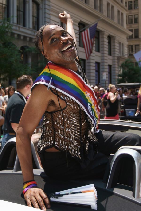 A man in a car with a rainbow sash. 