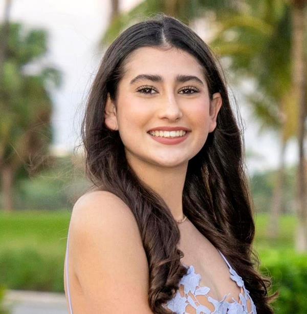 Ella Adler smiles, with her long, dark brown hair curled, and resting over her shoulders