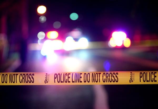 Night shot with police car lights in the background and yellow police line tape in the foreground.