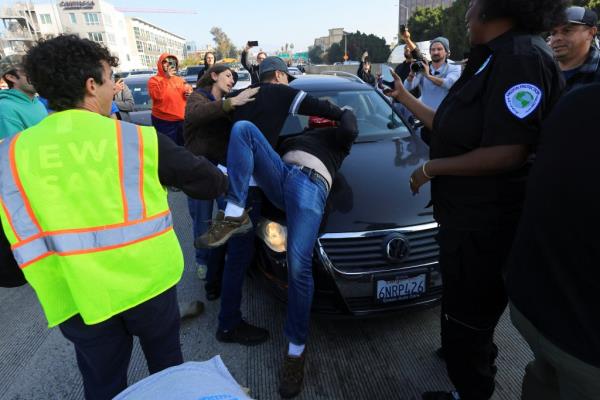 A man pinning a protester to a car on the freeway. 