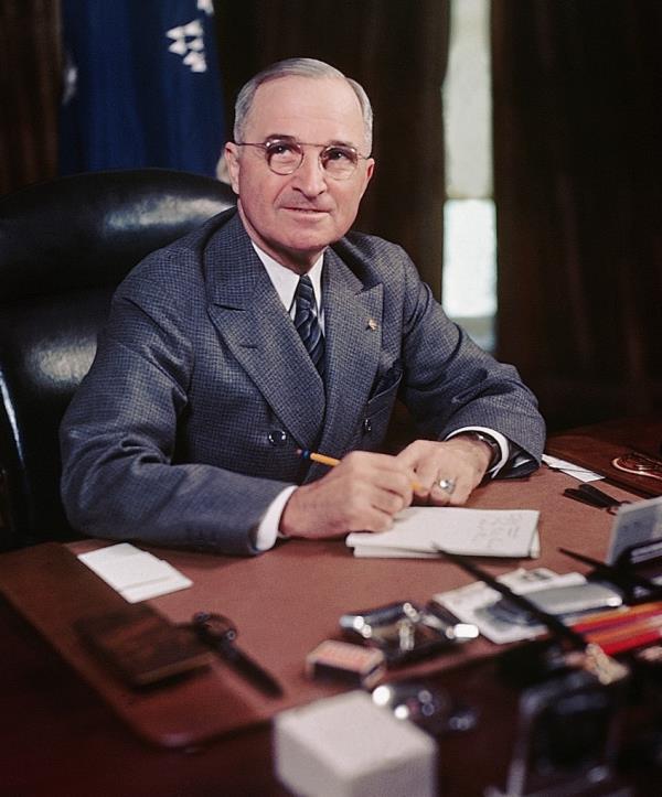 Harry Truman sitting at desk with paper and pencil. 