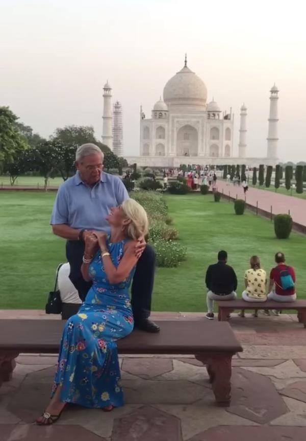 Bob Menendez standing in front of the Taj Mahal with his foot on a bench. Sitting on the bench is a blo<em></em>nde woman, turned backwards and holding his right hand while she looks into his eyes. 