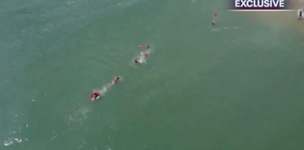 Other lifeguards swim out to meet the first lifeguard and help with the rescue.