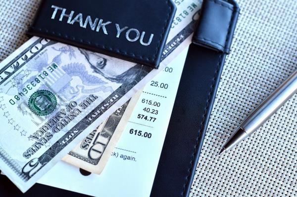 Top view of a wallet with cash, pen and food receipt bill on a table.