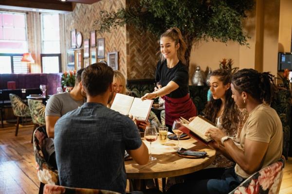 A multi-ethnic group of friends being served menus by a waitress in a restaurant