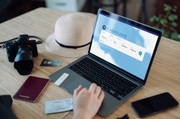 Cropped hand of woman shopping o<em></em>nline for flight tickets on airline website with laptop. Carried out Coro<em></em>navirus rapid self test, negative rapid lateral flow test device and travel essentials on table. Planning for travel. Travel during pandemic concept