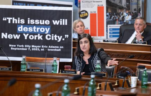 A woman speaking at a podium during US House Natural Resources Committee hearing on migrant camp proposal at Floyd Bennett Field in NY.