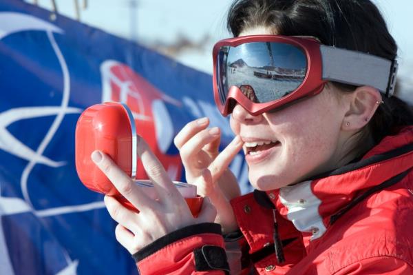 Attractive sport girl snowboarder applying face pack outdoors in winter mountain