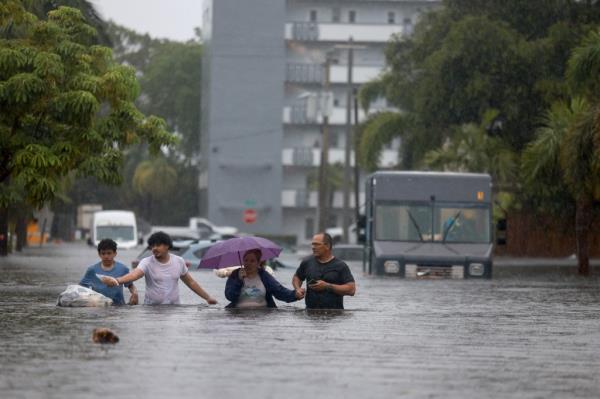 People walk through a flooded street as they evacuate on June 12, 2024, in Hollywood, Florida.