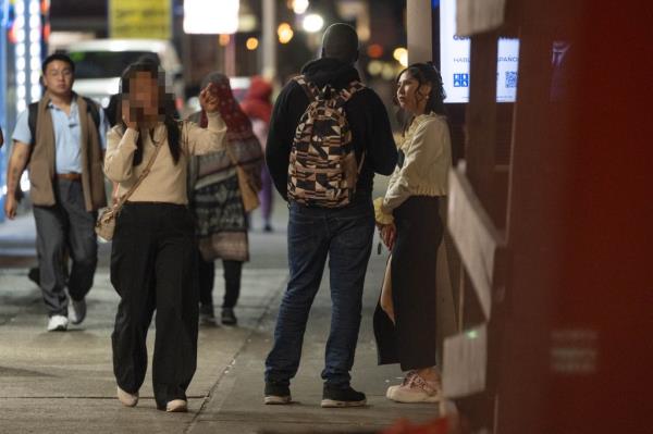 An apparent prostitute soliciting people on the sidewalk of Roosevelt Avenue, Queens, NY, amidst police crackdown due to community complaints.