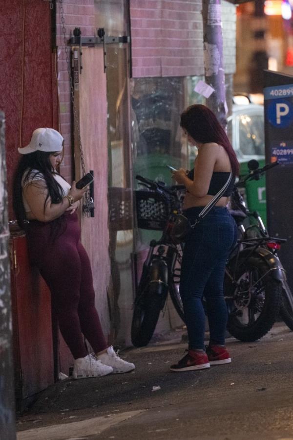 Prostitutes looking at their pho<em></em>nes while standing on Roosevelt Avenue