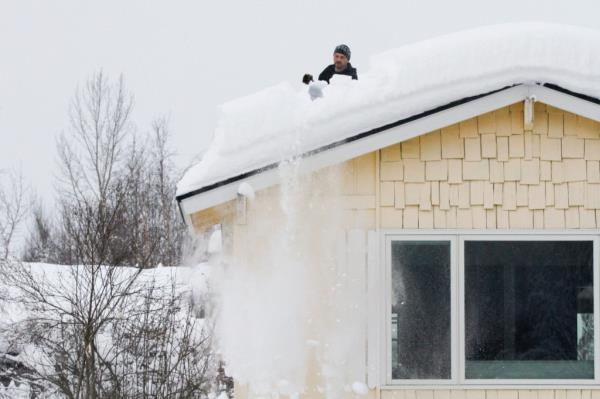 A man shoveling snow off his roof. 