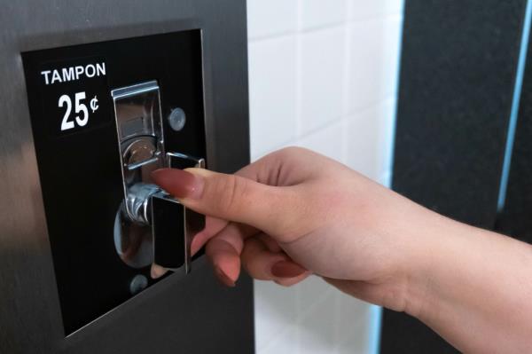 Woman inserting a coin into a tampon dispenser machine in a washroom