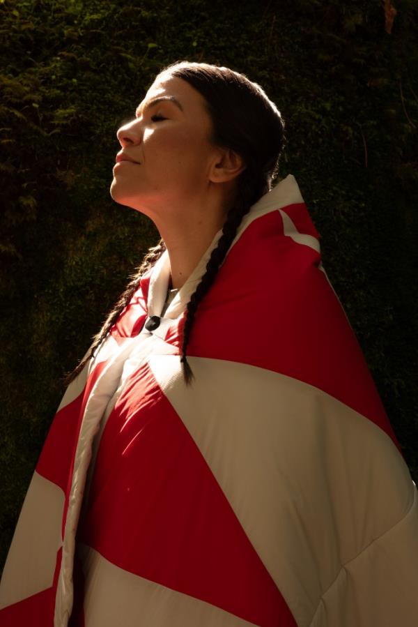 Woman wrapped in a blanket, eyes closed, demo<em></em>nstrating a collection inspired by Coast Salish spring and summer traditions