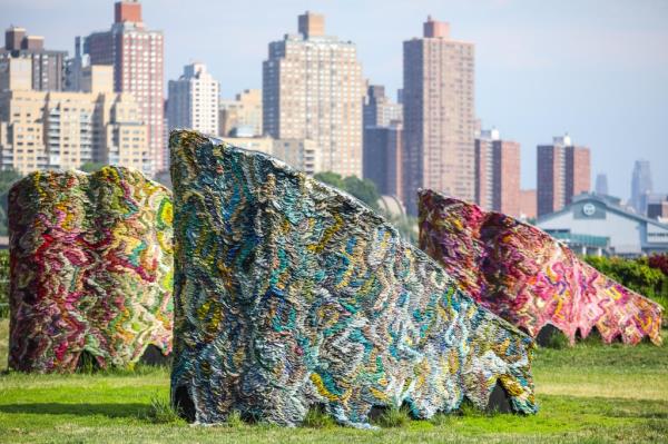 Vibrant art pieces by Suchitra Mattai displayed in a field at Socrates Sculpture Park, with a cityscape in the background