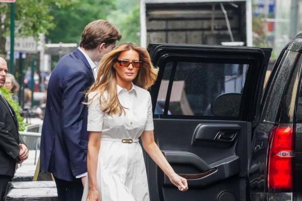 Former First Lady, Melania Trump, in a white dress and sunglasses, exiting Trump Tower with her son, Barron Trump, behind her.