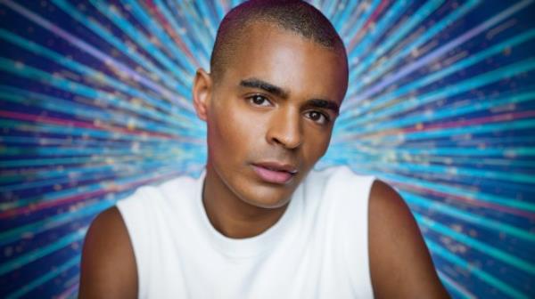 A press photo of Layton Williams, as a co<em></em>ntestant co<em></em>nfirmed for Strictly Come Dancing 2023. The Strictly branding is behind him, and the photo is from his chest up, and he's wearing a white vest.