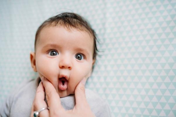 Baby with funny face, mother's Hand pressing her cheek