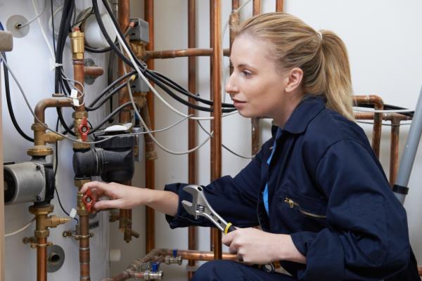 Female plumber working on heating boiler.