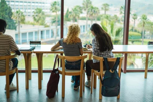 Young students studying inside university library, focusing on girls' backs