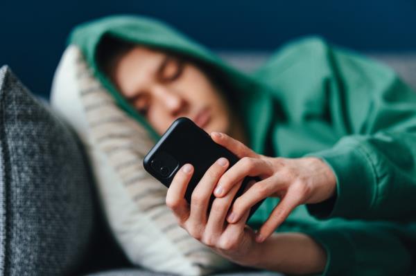 A teenager using a mobile phone lying on a couch at home.