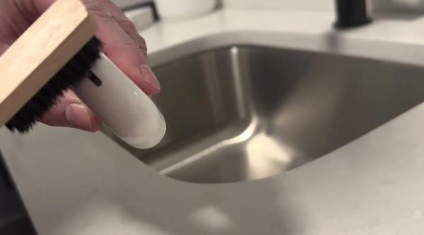 A hand holding a brush over a sink.