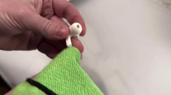 A close-up of a white AirPod being held by a hand.