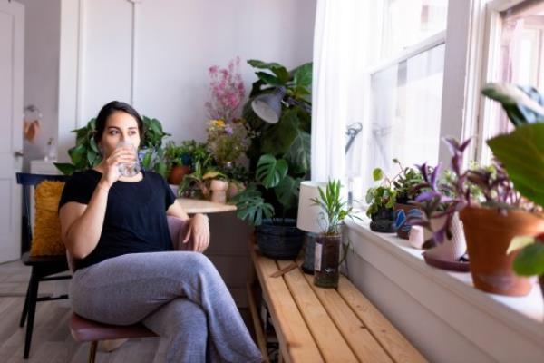 Young Adult Woman Sitting By A Window Drinking From A Glass Of Water