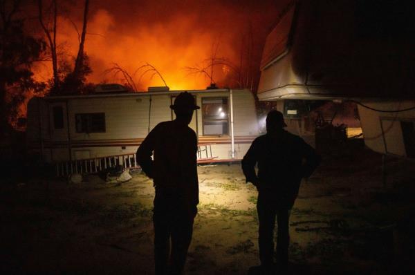 Firefighters stand in front of RV home as fire rages in background