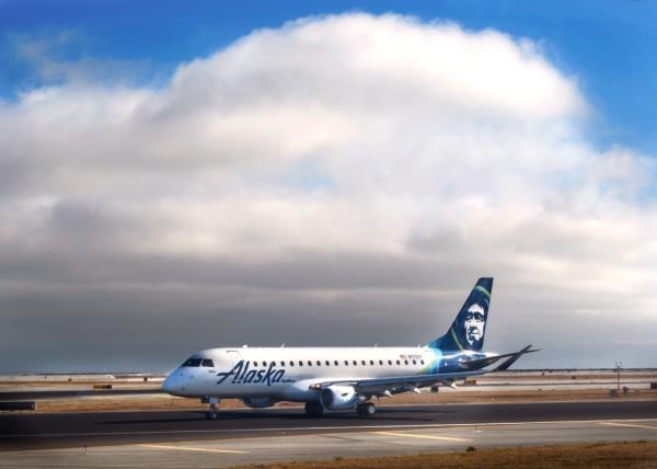 An Alaska Airlines plane sits on a runway with billowing gray clouds in the background,.