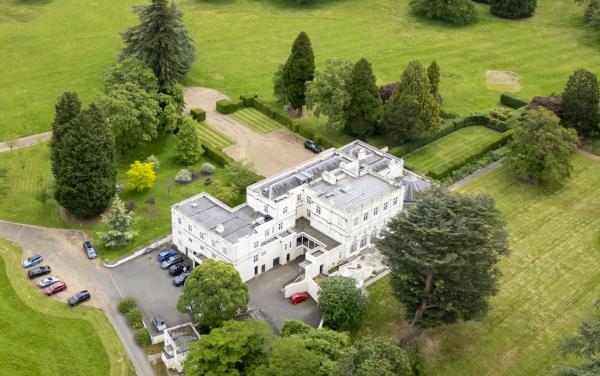 A large white building, known as the Royal Lodge in Windsor Great Park, surrounded by a parking lot and trees, the home of Prince Andrew and Sarah, The Duchess of York