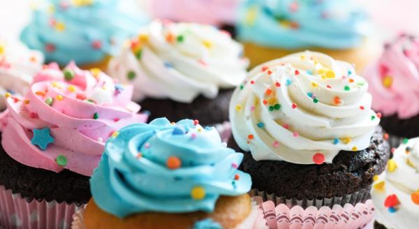 Close-up view of various cupcakes with pink, white, and blue cream and colorful sprinkles, prepared for a party or birthday celebration