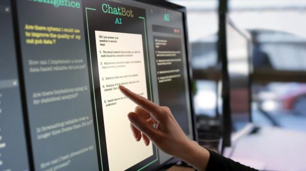 Woman's hand interacting with AI chatbot on touchscreen mo<em></em>nitor in open plan office