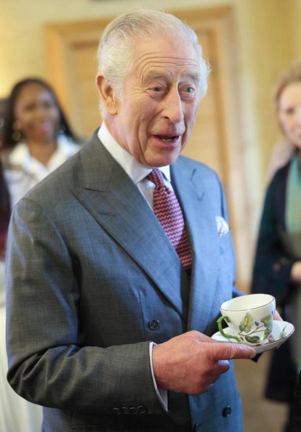 Britain's King Charles III reacts whilst holding a cup and saucer.